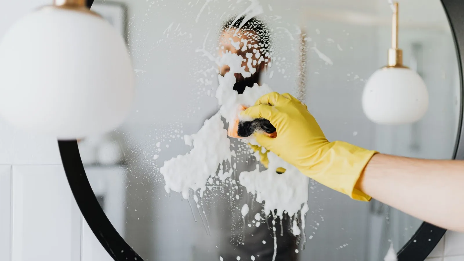 Gloved hand cleaning a bathroom mirror